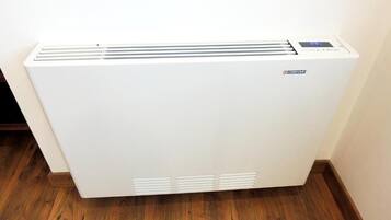 A white portable heater with a digital display and control panel, placed on a wooden floor against a wall.