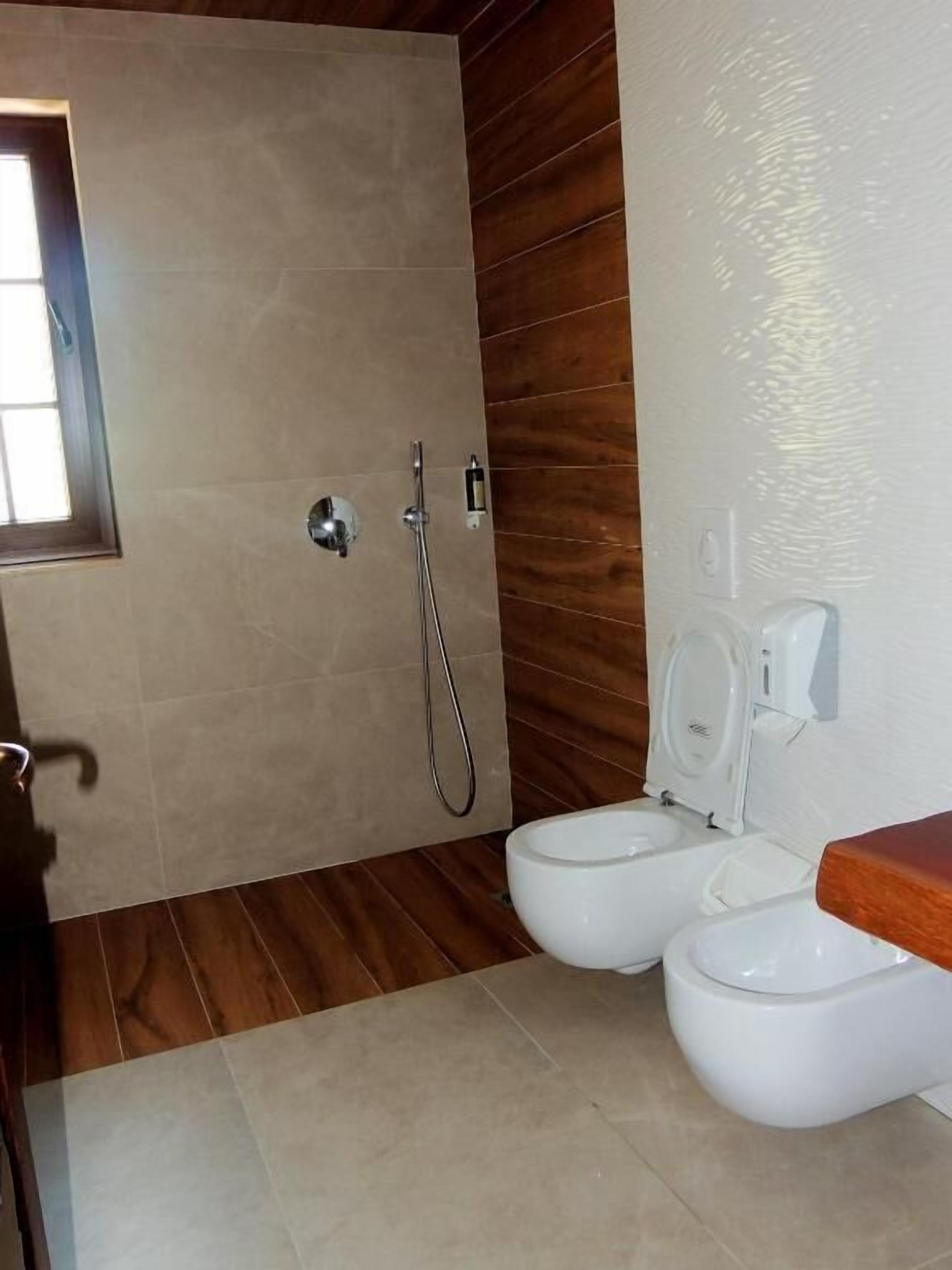 Une salle de bain avec une douche, deux toilettes et un mur en bois.