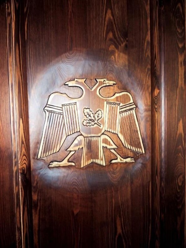 A wooden wall with a carved emblem featuring a shield and a flower.