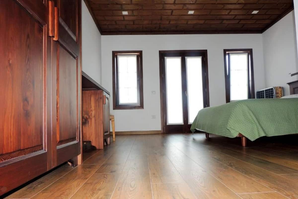 A room with wooden flooring, a bed with a green bedspread, and a wooden wardrobe.