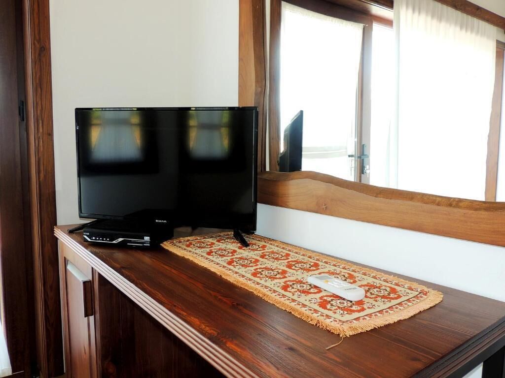 Un banc en bois, avec une télévision et une télécommande posées dessus, et un tapis à motifs sur le sol.