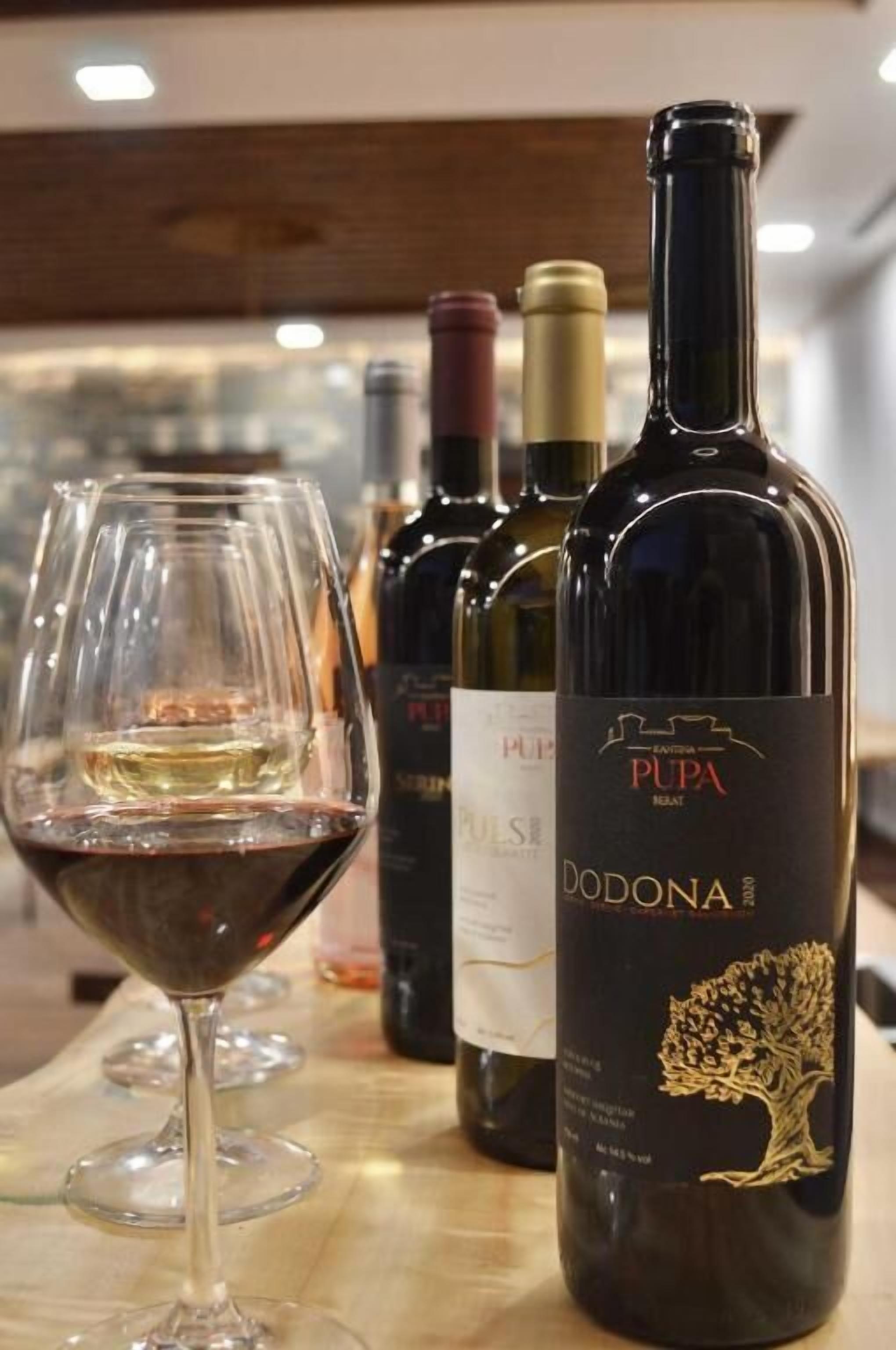 A wine glass filled with white wine and several wine bottles on a table.