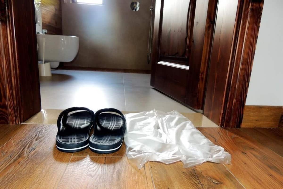 A wooden floor with a pair of black flip-flops and a white plastic bag.
