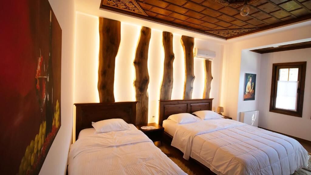 A hotel room with two beds, wooden headboards, and a large painting on the left wall.
