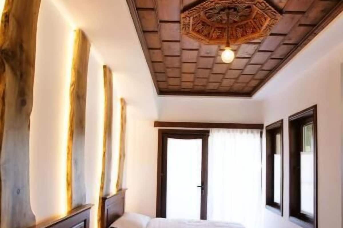 A bedroom with two beds, wooden ceiling beams, and a large wooden trunk against the wall.