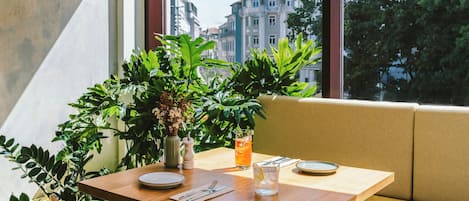 Una mesa de comedor con platos, cubiertos y un vaso de té helado, frente a una ventana con vista a la ciudad.