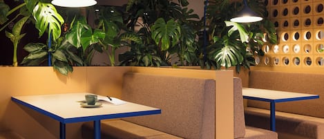A seating area with two tables and benches, surrounded by lush green plants and a perforated wall.