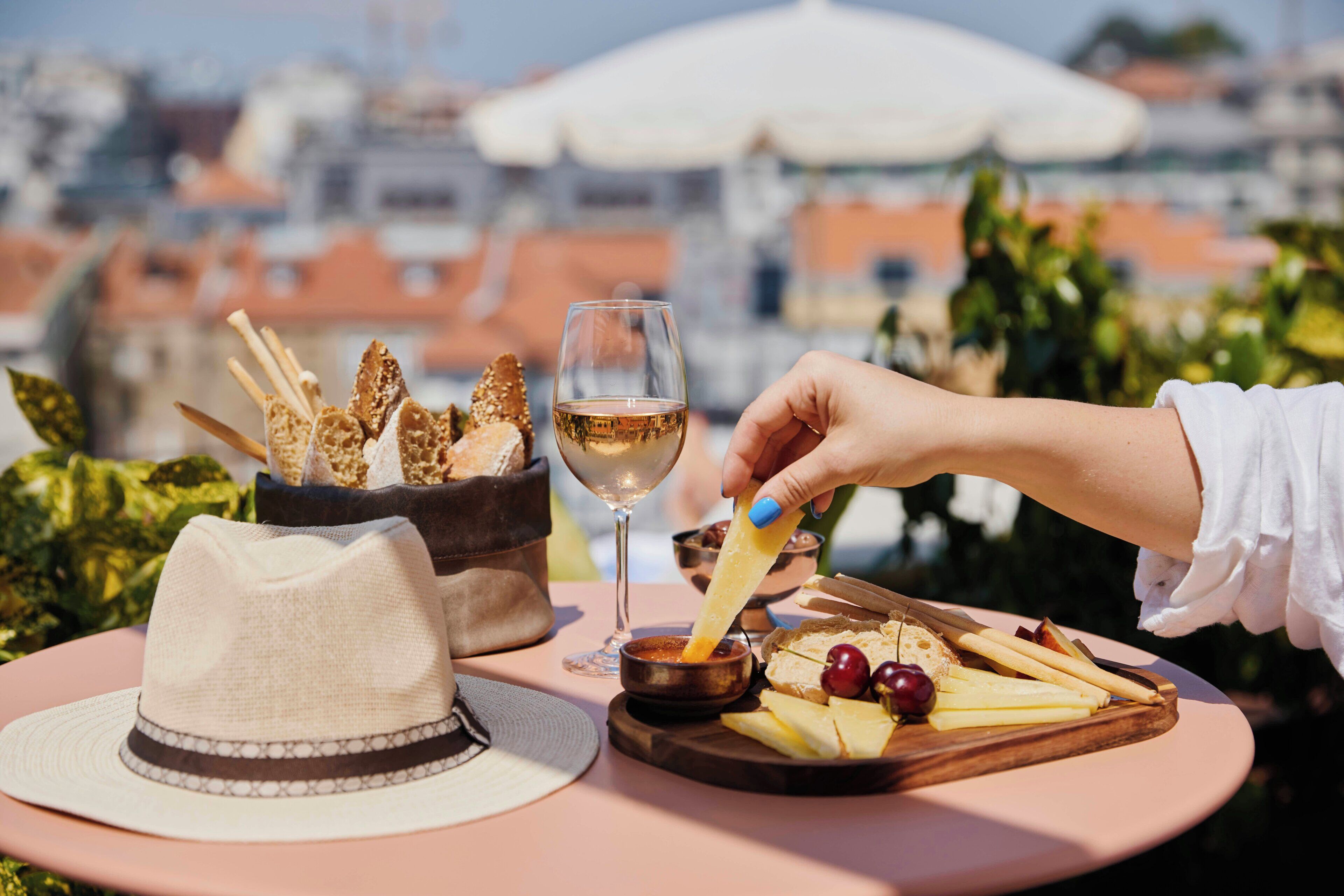 A table with a hat, a glass of wine, and a cheese board with crackers.