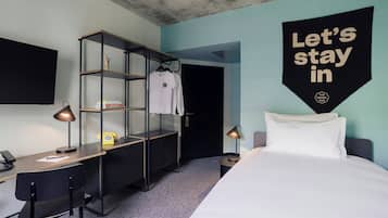 Une chambre d’hôtel avec un lit, un bureau, une chaise, une armoire et une pancarte indiquant : « Restons à l’hôtel ».
