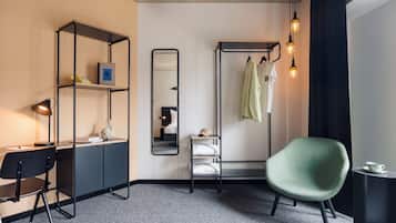 A modern hotel room with a desk, chair, wardrobe, and a green armchair.