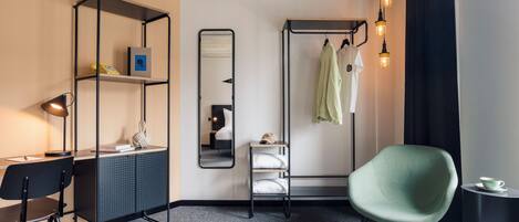 A modern hotel room with a desk, chair, wardrobe, and a green armchair.