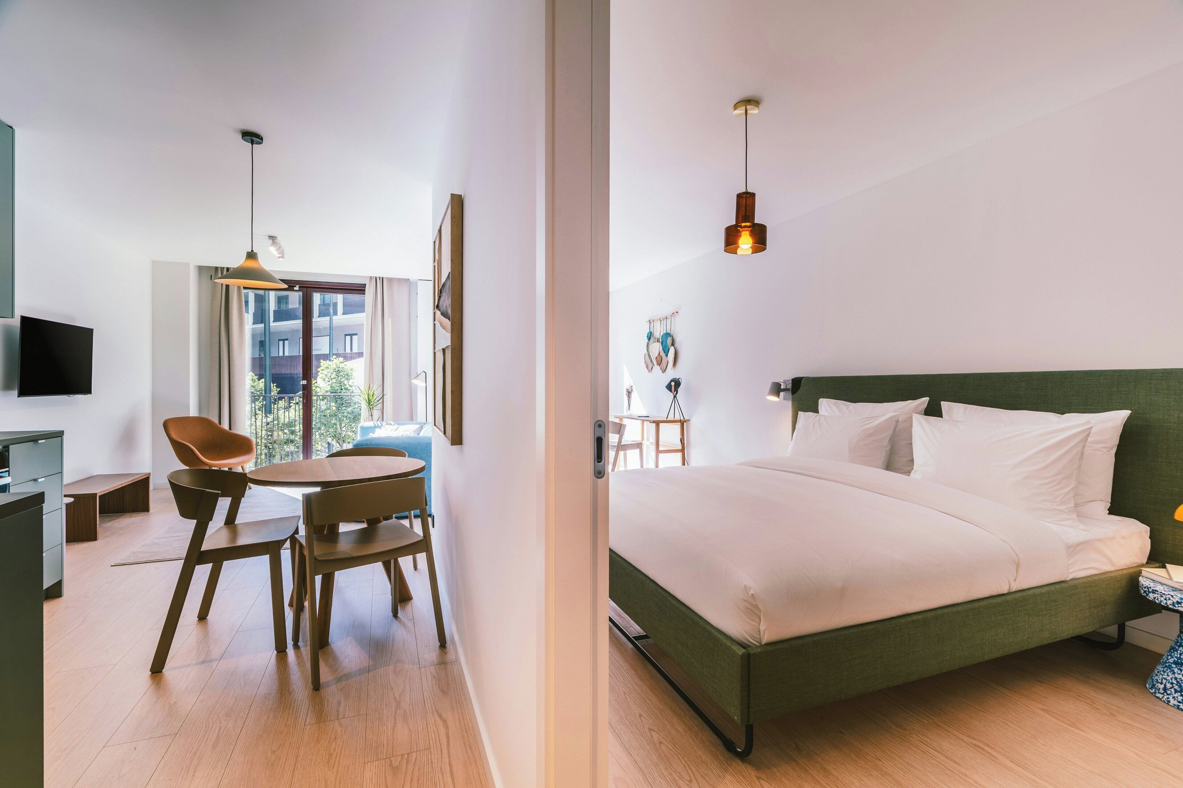 Een moderne hotelkamer met een bed, een bureau met stoel, een eettafel en uitzicht op het omliggende landschap.