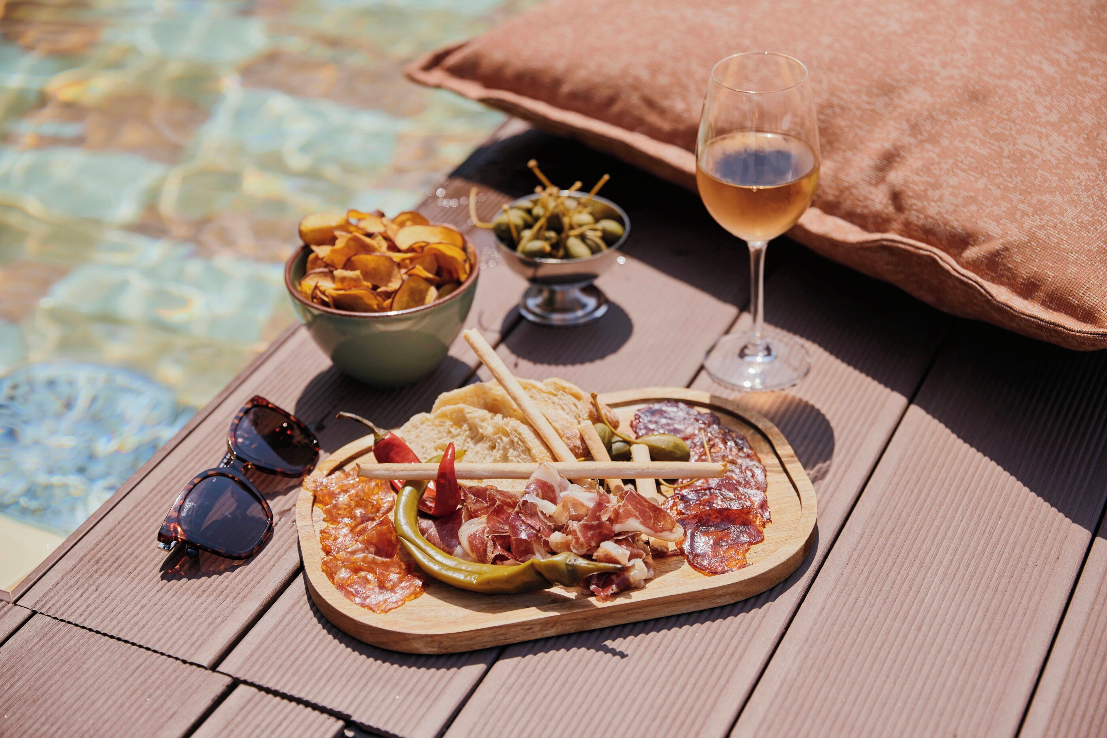 Una mesa de madera con una bandeja de comida, una copa de vino y unas gafas de sol.
