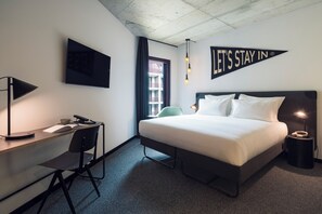 A modern hotel room with a bed, desk, chair, and a "LET'S STAY IN" sign. - The Social Hub Porto (Porto)