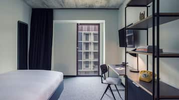 A hotel room with a bed, desk, chair, and a bookshelf.