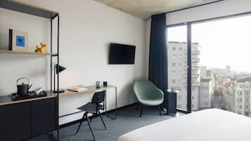 Habitación de hotel con cama, escritorio, silla, televisión y vista de la ciudad.