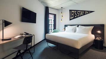 A hotel room with a bed, desk, chair, TV, and a sign that says 'LET'S STAY IN'.