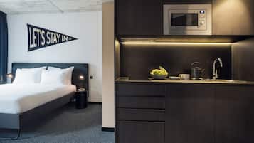 Quarto de hotel moderno com uma cama, um espaço de cozinha compacto com micro-ondas e uma placa com a inscrição "LET'S STAY IN".