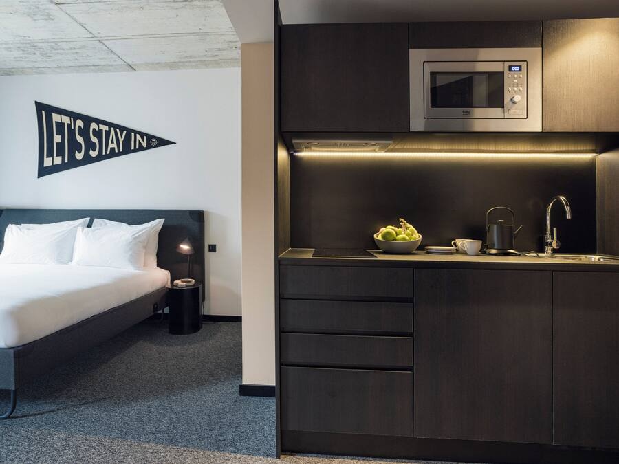 Quarto de hotel moderno com uma cama, um espaço de cozinha compacto com micro-ondas e uma placa com a inscrição "LET'S STAY IN".