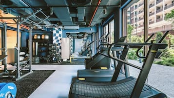 Une salle de sport équipée de matériel d’exercice, d’un tapis de course et offrant une vue sur un bâtiment à l’extérieur.