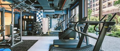 Un gimnasio con equipo de ejercicio, cinta de correr y vistas a un edificio cercano.