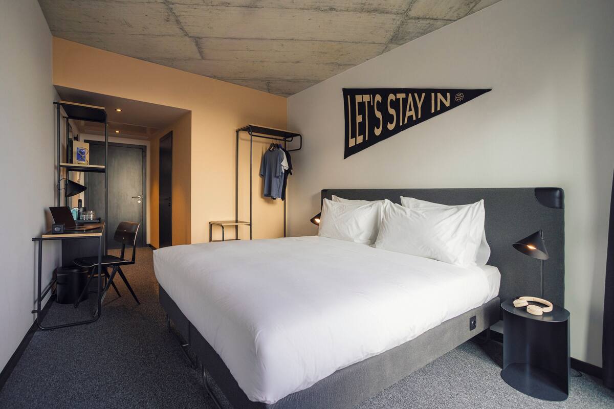 A hotel room with a large bed, a desk with a laptop, a chair, and a coat rack.