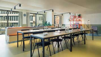 A conference room with a long table, chairs, a red shelving unit, and a clock on the wall.