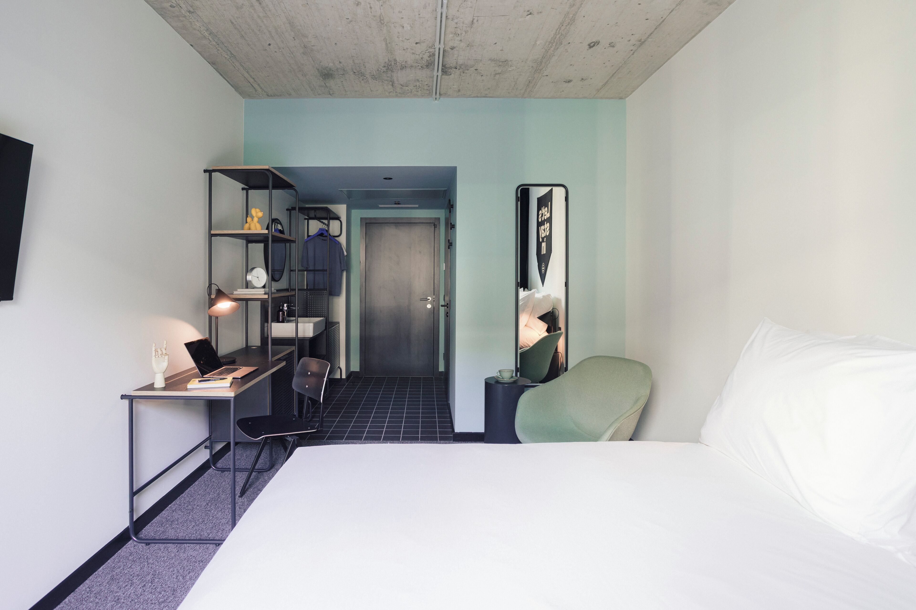 A hotel room with a bed, desk, chair, and a small seating area.
