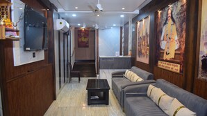 A hotel reception area with a reception desk, a sofa, a coffee table, and a wall-mounted television. - Hotel shri shankar (Varanasi)