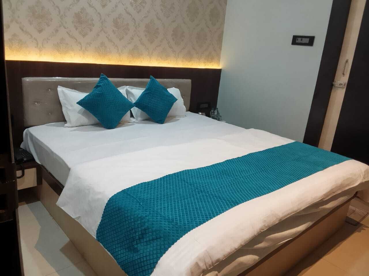 Un lit bien fait, recouvert d’une couvre-lit blanche et turquoise, avec deux oreillers turquoise et une tête de lit ornée d’un papier peint à motifs de couleur claire.