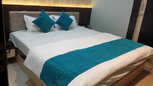 A neatly made bed with a white and teal bedspread, two teal pillows, and a headboard with a light-colored patterned wallpaper. - Hotel shri shankar (Varanasi)