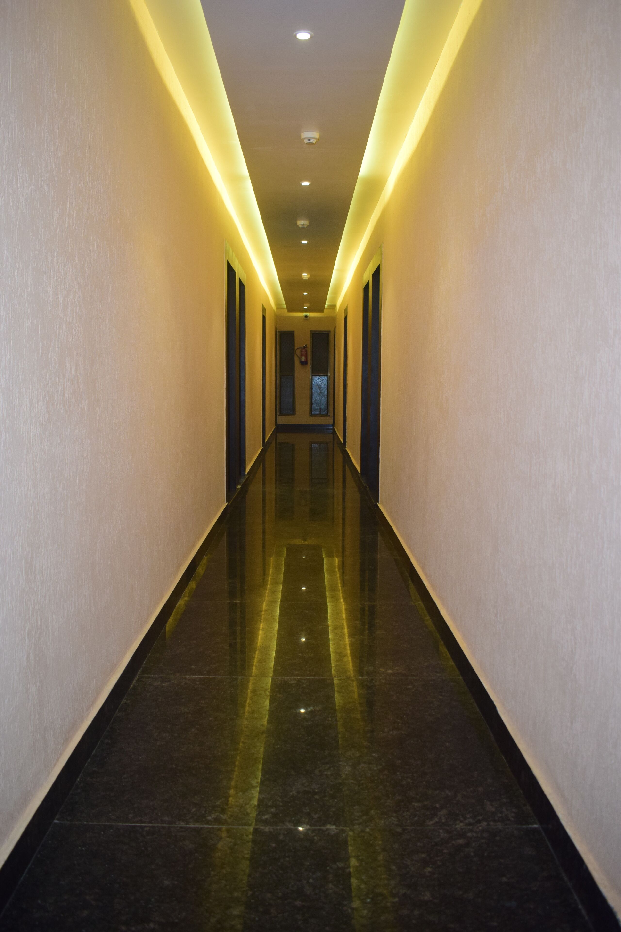 A long, narrow hallway with a reflective floor and walls, illuminated by overhead lights.