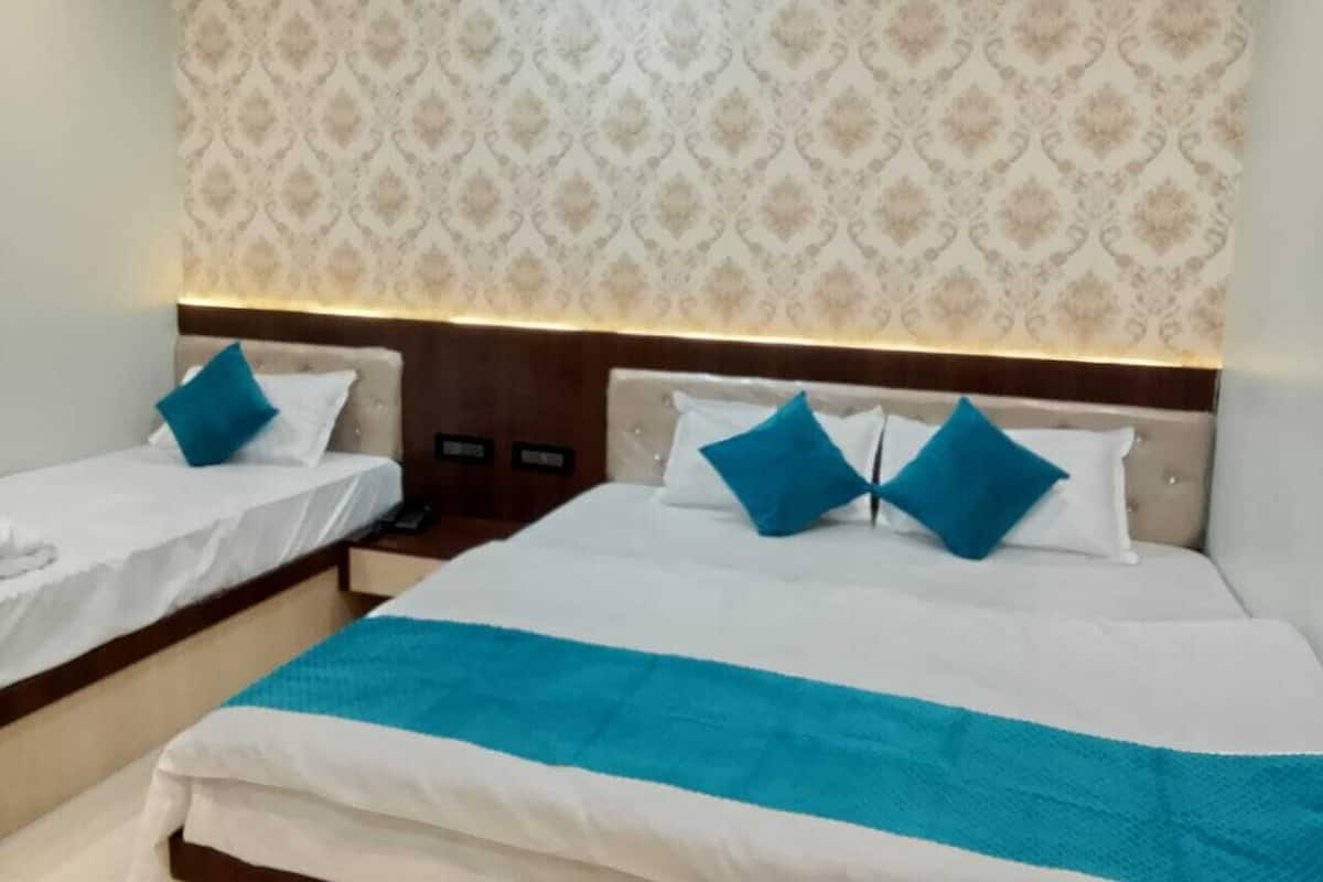 Habitación de hotel con dos camas, cada una con una almohada azul decorativa y una colcha blanca. La habitación tiene papel tapiz estampado y un cabecero de madera.