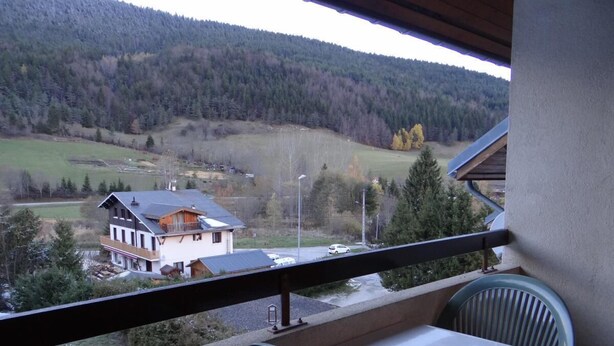 Un balcon avec une table et des chaises, donnant sur une vallée où se trouvent une maison et des arbres.