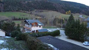 Un quartier résidentiel avec une maison à deux étages dotée d’un balcon, entourée d’arbres et s’ouvrant sur un paysage vallonné en arrière-plan.