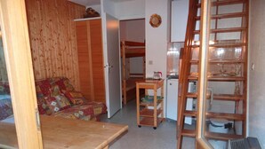 Une petite pièce comprenant un lit superposé, une table en bois et un coin cuisine.