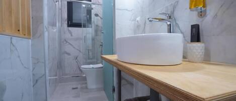 Une salle de bain moderne avec un lavabo blanc, des murs en marbre et une cabine de douche en verre.