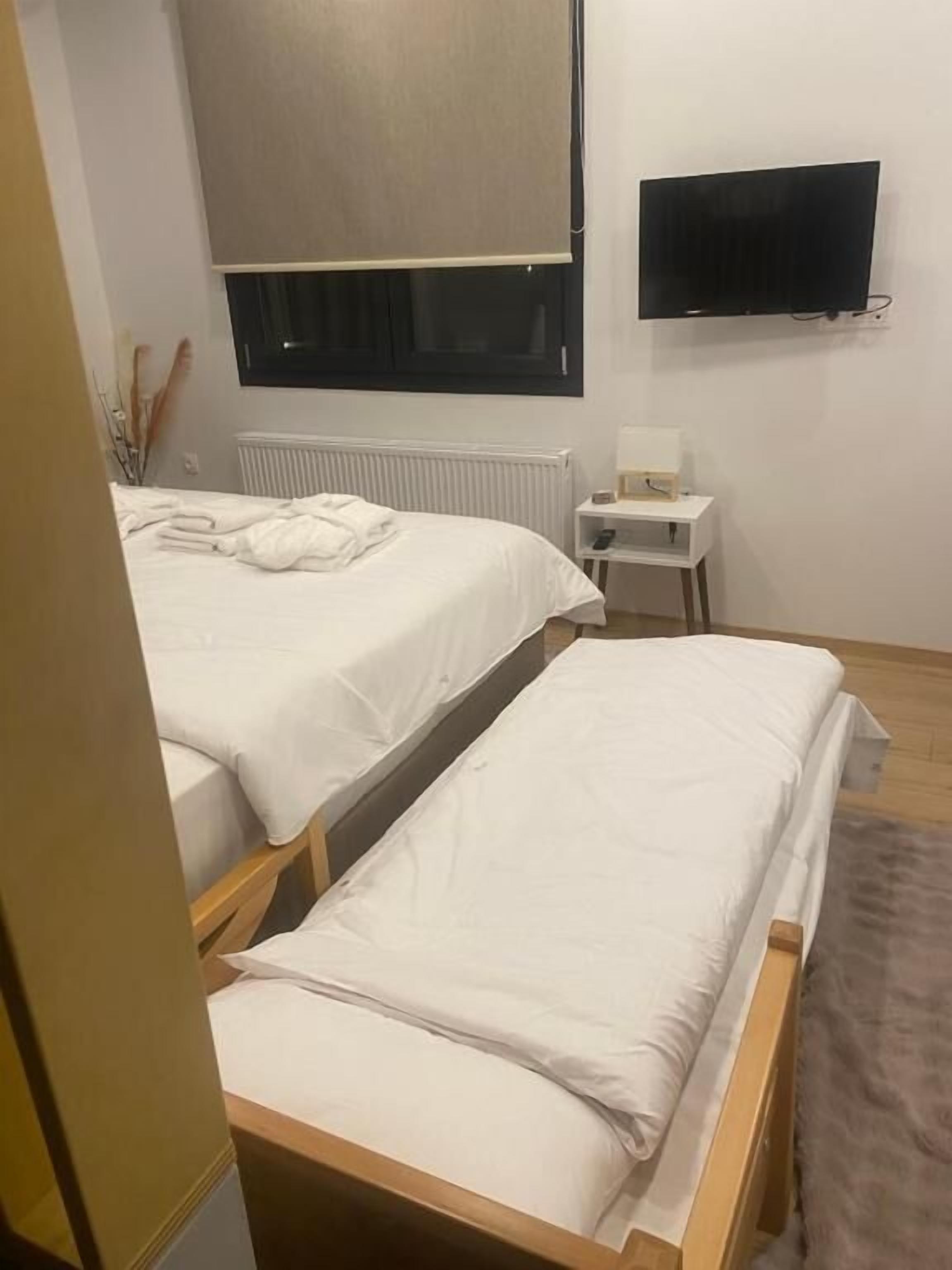A hotel room with two single beds, a small bedside table with a lamp, a TV mounted on the wall, and a radiator.