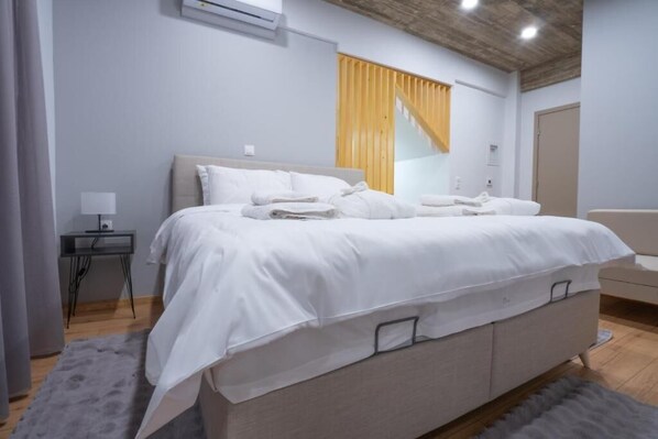 A modern bedroom with a large bed, a bedside table, and a chair. - The Rooms (Almopia)