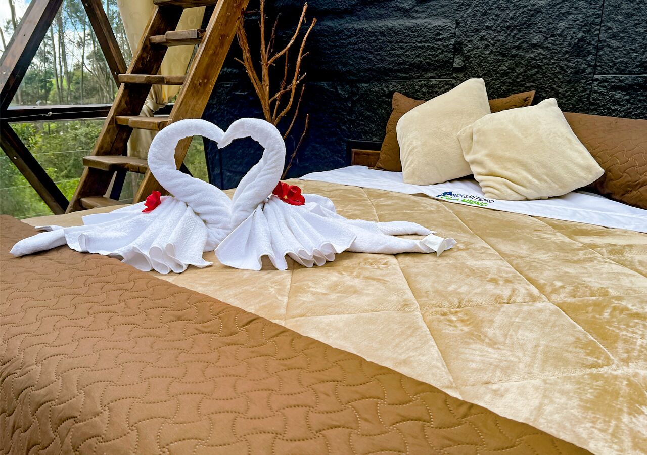 Uma cama com cobertura marrom acolchoada, uma escada de madeira e uma toalha decorativa em formato de coração.
