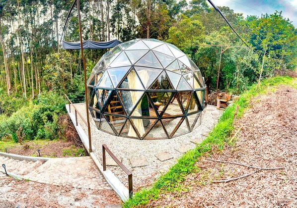 A geodesic dome structure with a wooden deck and stone pathway.