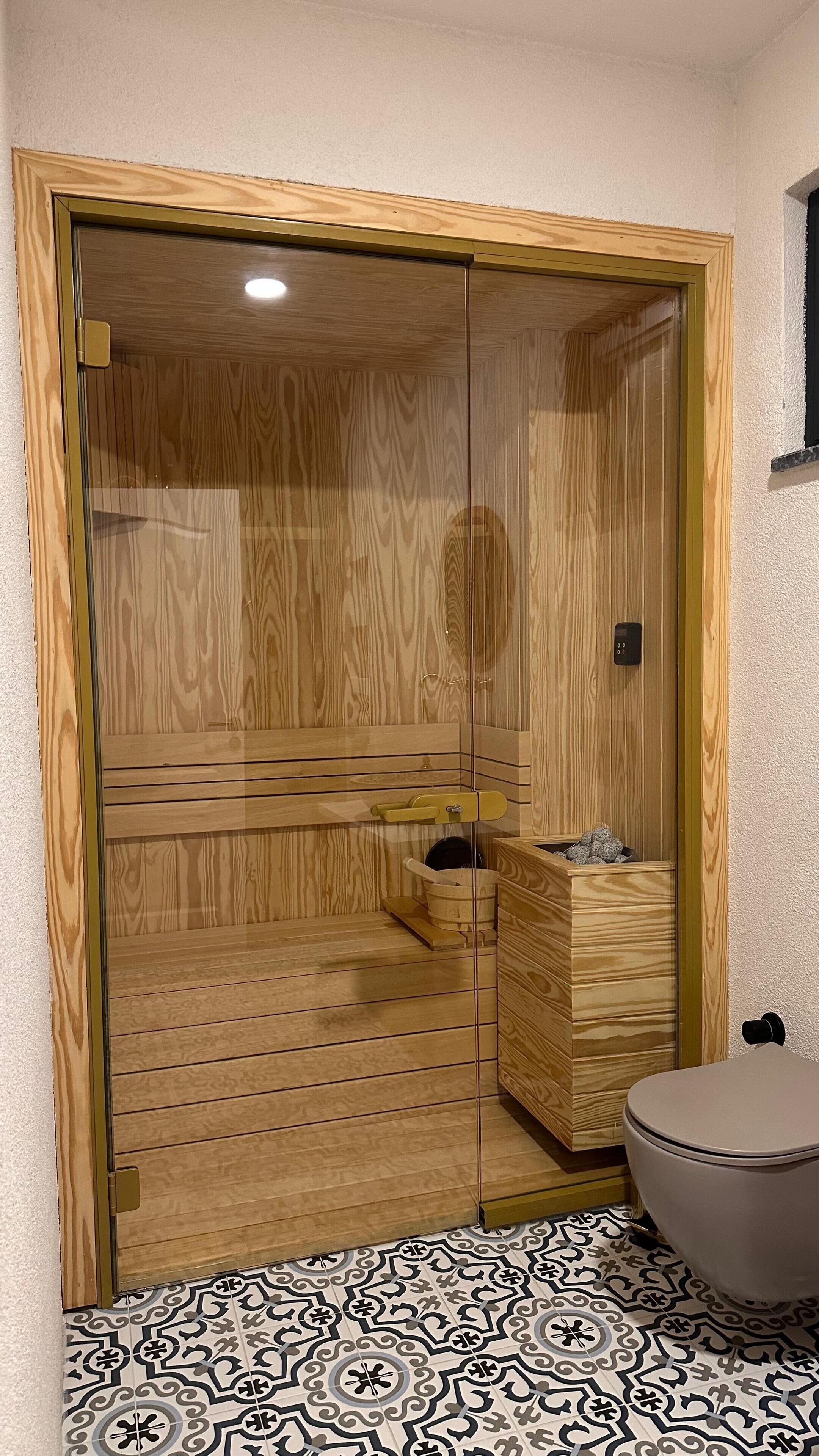 A wooden sauna with a glass door, a wooden bench, and a small wooden cabinet.
