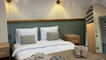 A neatly made bed with a towel and a bag, a wooden headboard, a wall-mounted air conditioner, and two wall sconces.