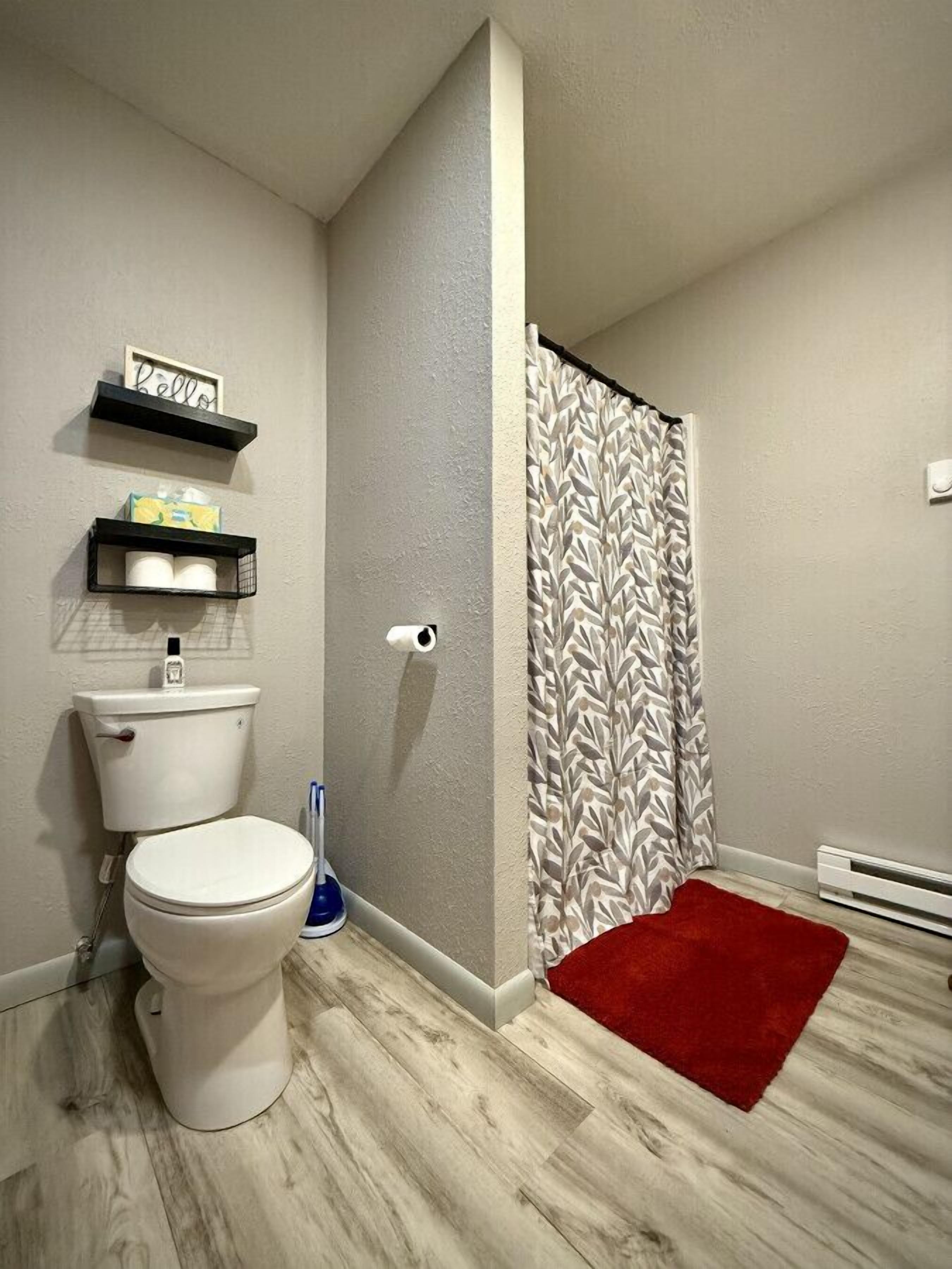 Ein Badezimmer mit Toilette, einer Duschvorhang, einem roten Teppich und Ablagen mit Pflegeprodukten.