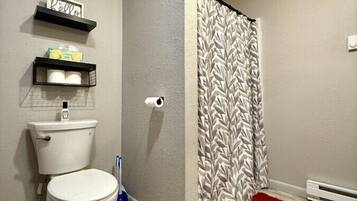 Ein Badezimmer mit Toilette, einer Duschvorhang, einem roten Teppich und Ablagen mit Pflegeprodukten.