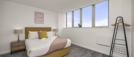 A modern bedroom with a large bed, a nightstand, a window with a view, and a radiator.