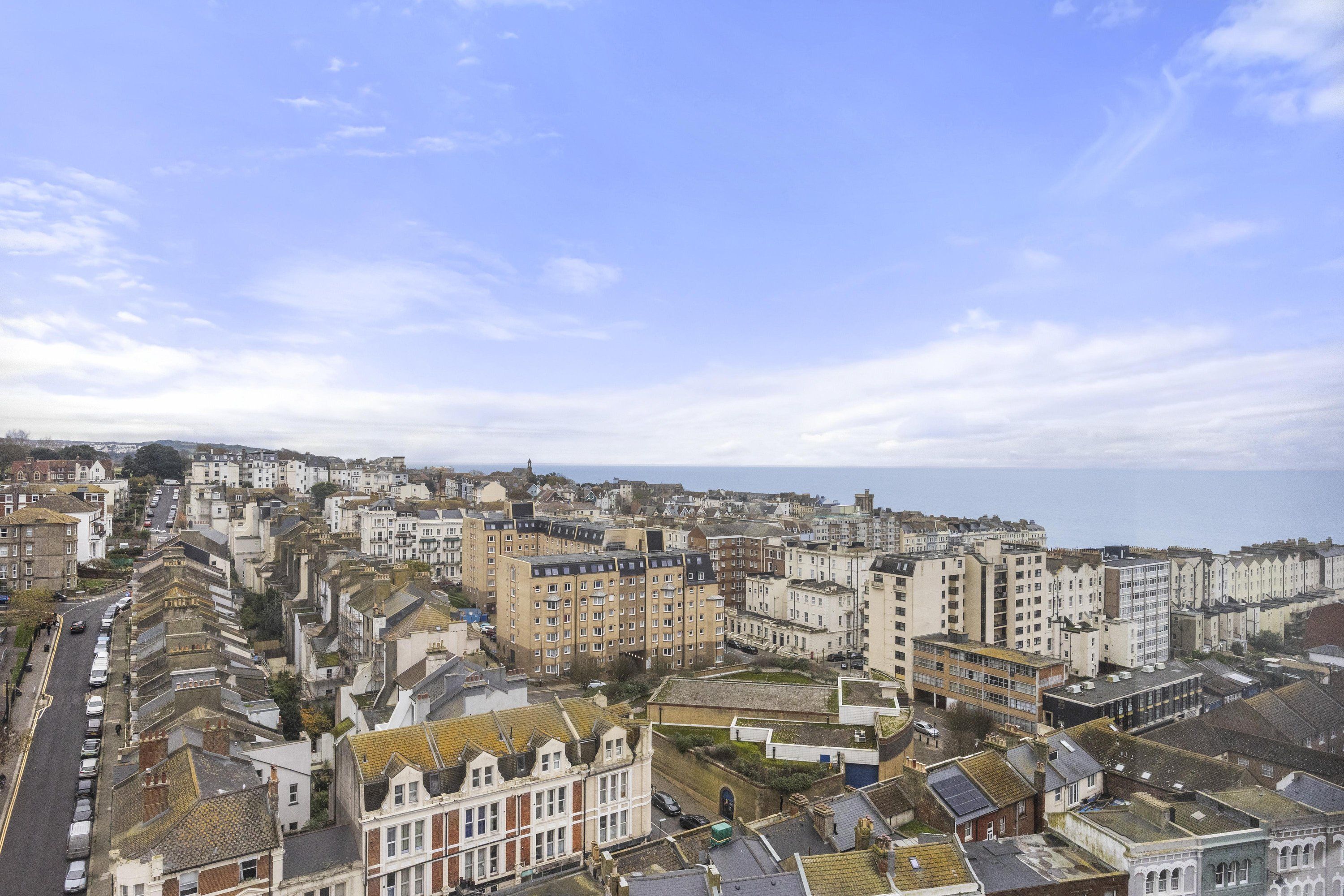 A coastal cityscape with a mix of residential and commercial buildings, a prominent road, and a view of the sea.
