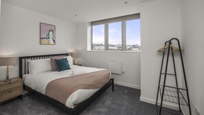 Een slaapkamer met een bed, nachtkastjes, een raam met uitzicht over de stad en een ladder tegen de muur.