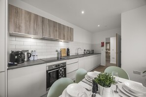 A modern kitchen with white cabinets, a black countertop, and a dining area with green chairs and white plates. - Ocean View B Free Parking By My Getaways (St Leonards-On-Sea)