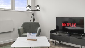 Een moderne kamer met een grijze fauteuil, een witte tafel en een televisie waarop 'NETFLIX' staat.